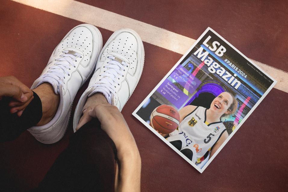 Weiße Sneakers stehen neben einem LSB Magazin, das auf einem Basketballfeld liegt.